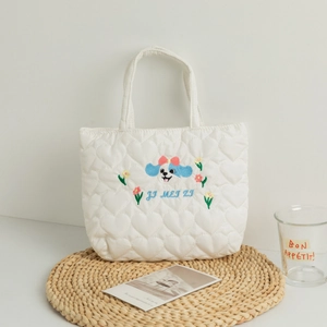 Close-up of white heart-quilted tote bag featuring blue puppy embroidery and top handles