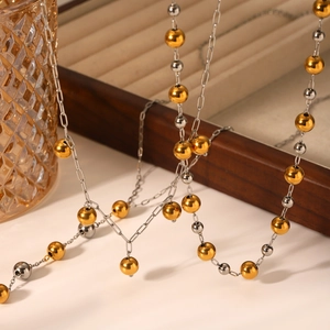 Two-tone stainless steel beaded necklace with gold and silver balls on a wooden tray
