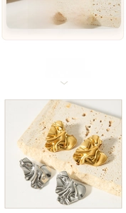 Detailed close-up of wrinkled heart earrings in polished gold and silver metal finishes