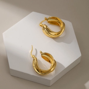 Golden croissant twist hoop earrings with mirror finish on white geometric display