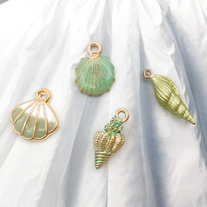 Close-up of shell-shaped green enamel pendants with gold finish on fabric