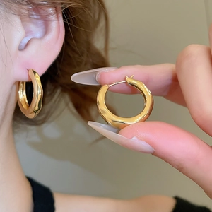 Detail of 18K gold-plated textured round hoop earring worn on model ear and held by hand