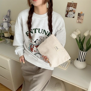 Close-up of beige corduroy cosmetic pouch held by a hand in a cozy lifestyle setting