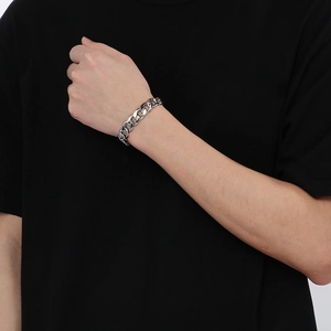 Gros plan sur un bracelet gourmette argenté porté au poignet sur un t-shirt noir
