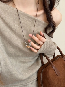 Detail of a vintage wooden horse pendant on a leather cord worn with a beige knit sweater