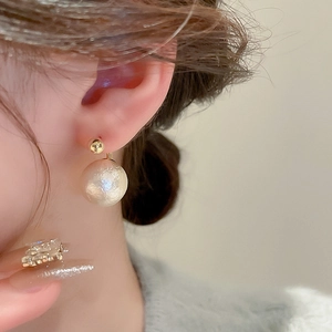 Détail d'une boucle d'oreille dorée avec perle texturée sur l'oreille du mannequin