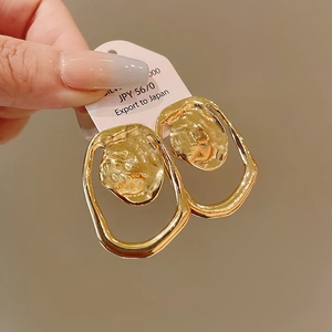Detail of gold geometric hollow earrings with hammered texture held on display card