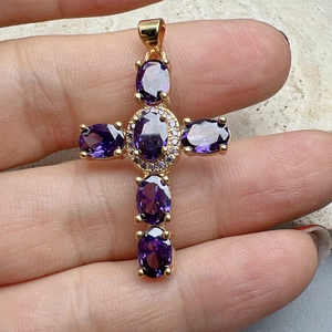 Detail of gold cross pendant with five oval purple stones held by hand to show size