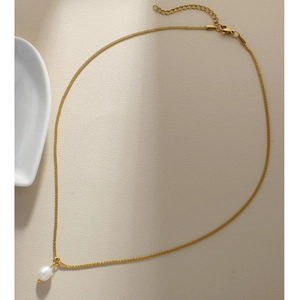Close-up of a gold freshwater pearl pendant necklace on a beige textured surface