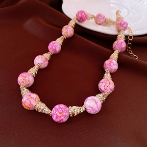 Vista macro di perle di marmo rosa vintage con accenti dorati in strass e catena regolabile