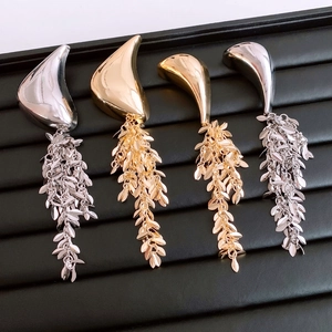 Detail of geometric metal pins with gold and silver finishes featuring cascading leaf tassels