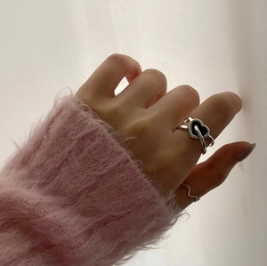 Detail of layered 925 silver heart and wave rings worn against a soft pink sweater