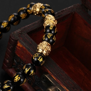 Détail de perles en onyx noir avec mantra doré et breloque Pi Xiu sur une boîte en bois
