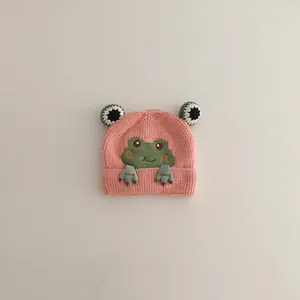 Close-up of pink knit baby hat featuring green frog embroidery and soft striped texture