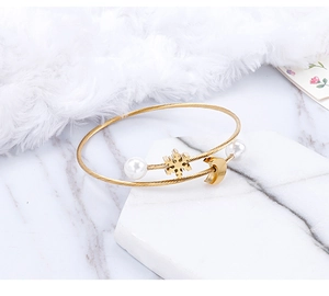 Detail of gold open bangle with white pearl snowflake and moon charms on marble