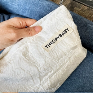 Detail of white jacquard cosmetic bag featuring 3D floral texture and a woven brand label