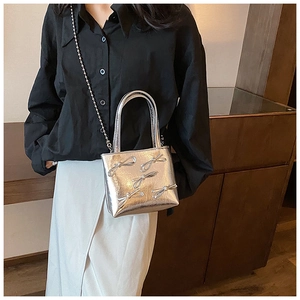 Detailed view of silver textured square handbag with metallic bows and chain strap