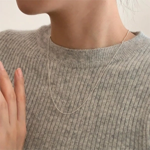 Detail shot of minimalist silver bead chain necklace worn on model with grey knit sweater