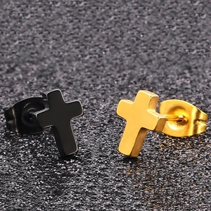 Detailed macro view of black and gold cross-shaped stainless steel stud earrings on textured surface