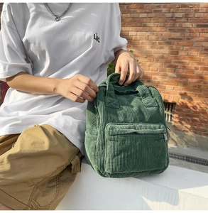 Detail des grünen Cord-Rucksacks mit weicher Textur und vorderem Reißverschlussfach
