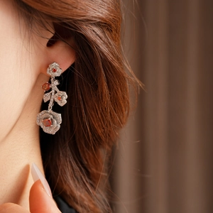 Close-up of vintage silver rose earrings with red gemstones and white diamonds on a model