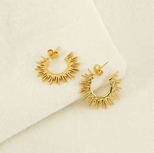 Detailed view of gold sunburst C-shaped earrings on soft beige linen fabric texture