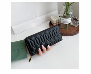 Close-up of elegant black quilted leather clutch wallet held by a model in a lifestyle setting
