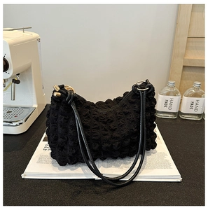Close-up of black bubble textured fabric shoulder bag on magazine with creative styling