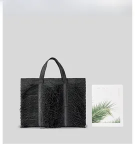 Size comparison of large black tassel woven tote bag next to a book for scale