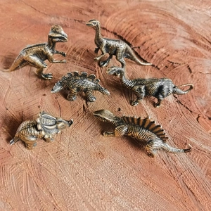 Detailed set of six miniature brass dinosaur figurines on natural wood background