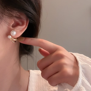 Close-up of elegant C-shaped gold earrings with double white pearls on model