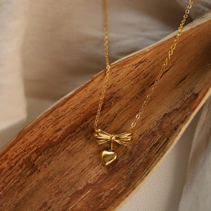 Macro detail of gold bow and heart pendant necklace on textured autumn leaf