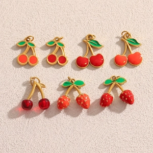 Macro view of cherry and strawberry pendants in gold-plated steel with red enamel details