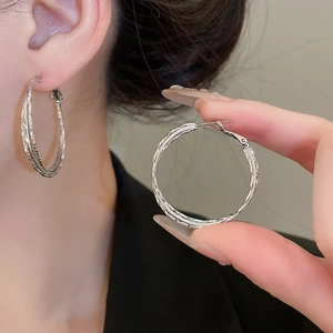 Detail view of multi-layered silver geometric hoop earrings on ear and in hand