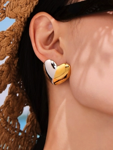 Close-up of dual-tone gold and silver heart stud earrings in outdoor sunlight
