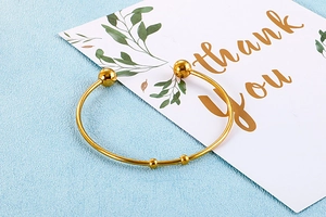 Close-up of a gold stainless steel open bangle with spherical ends on a card