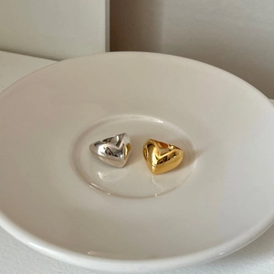 Detailed view of 3D polished gold and silver heart-shaped wide rings on ceramic dish