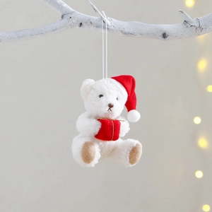 Plush Christmas bear ornament with red hat and gift box hanging on a white branch