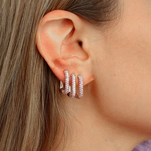 Close-up of rose gold rectangular earrings with purple zircons worn on earlobe