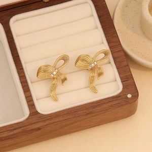 Detailed macro view of golden bow stud earrings with clear gems in a wooden box