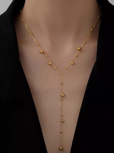 Detail of a minimalist gold layered Y-shaped necklace with delicate beads on a suit