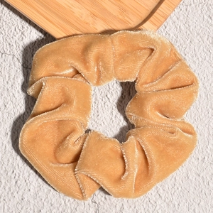 Detailed view of a golden velvet scrunchie with soft folds on a neutral textured background