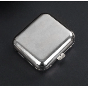 Elegante cenicero portátil de metal plateado con tapa abatible sobre un fondo negro