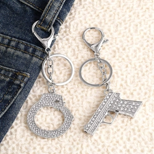 Hip hop style silver gun and handcuffs keychain set with white crystals on denim background