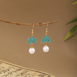 Close-up of green enamel flower earrings with white pearls hanging on a branch