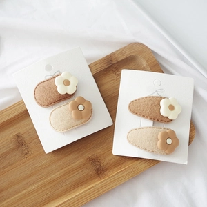 Detail of floral felt hair clips in milk tea colors on a display card and wooden tray