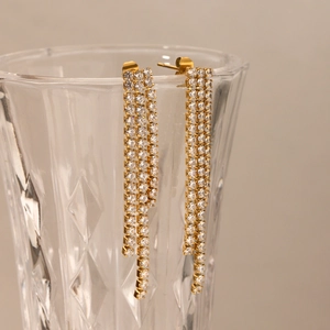 Detailed macro view of gold tassel earrings with zircon crystals hanging on a glass rim