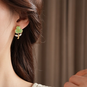 Close-up of gold flower earrings with green petals and zircon details worn by a model