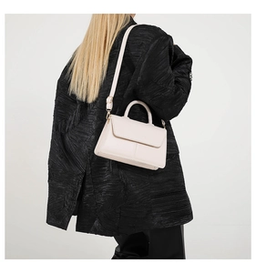 Close-up of minimalist beige PU leather shoulder bag worn over a black pleated jacket