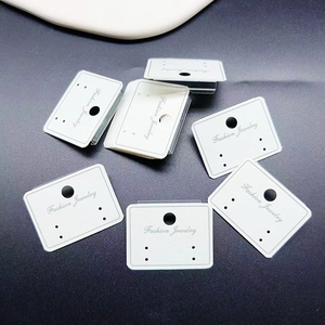 Close-up of white PVC earrings display card with Fashion Jewelry text on gray surface
